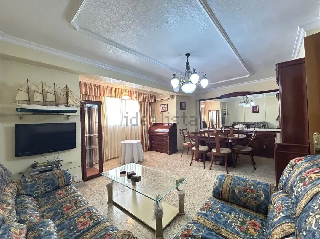 Sala de estar con sofás florales azules, mesa de centro de cristal y comedor visible al fondo.