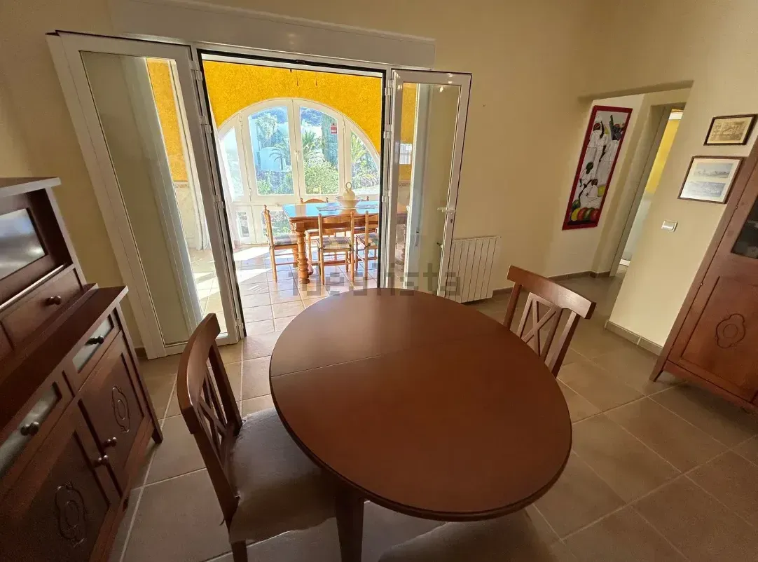 Comedor con mesa y sillas de madera, conectado a una zona de comedor exterior.