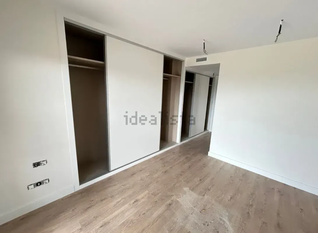 Dormitorio vacío con armario, puertas corredizas y suelo imitación madera.