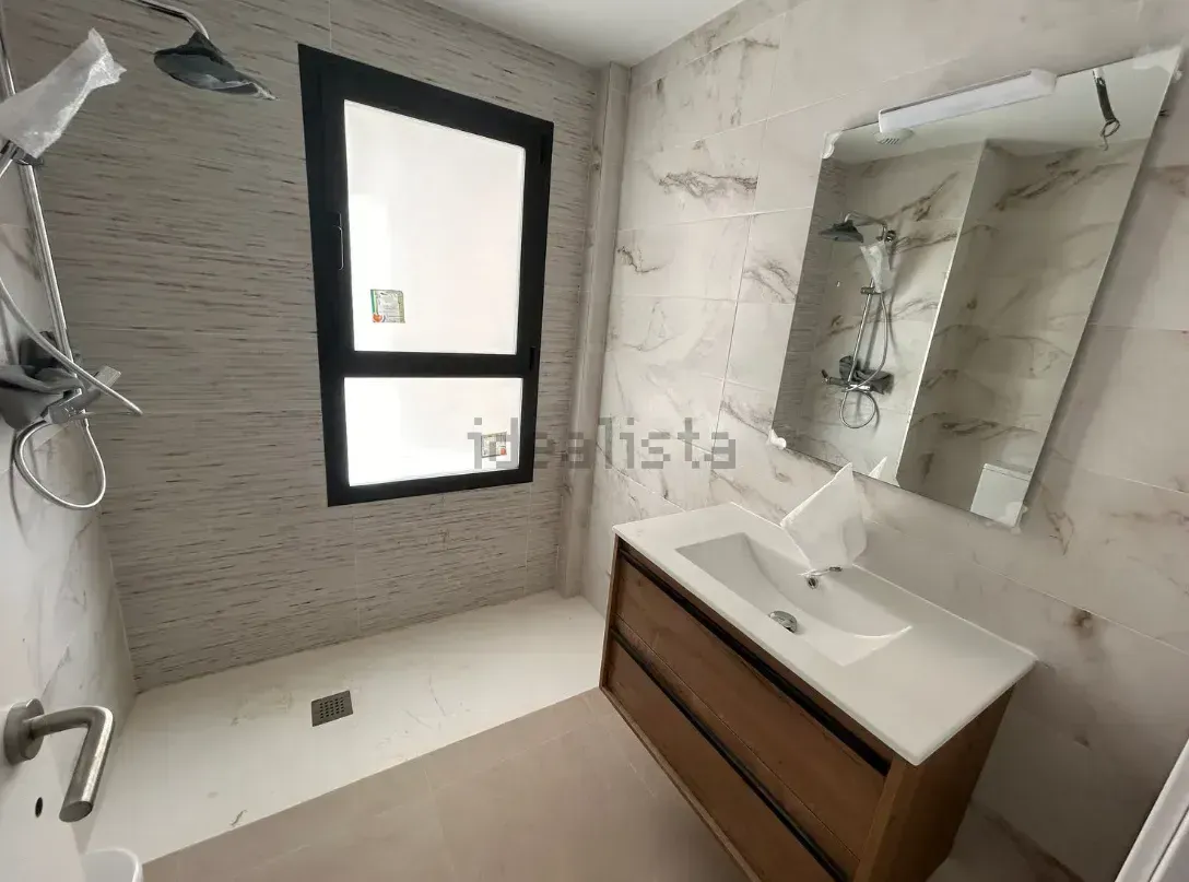 Baño con ducha, lavabo y ventana grande. Combinación de colores blanco y marrón.