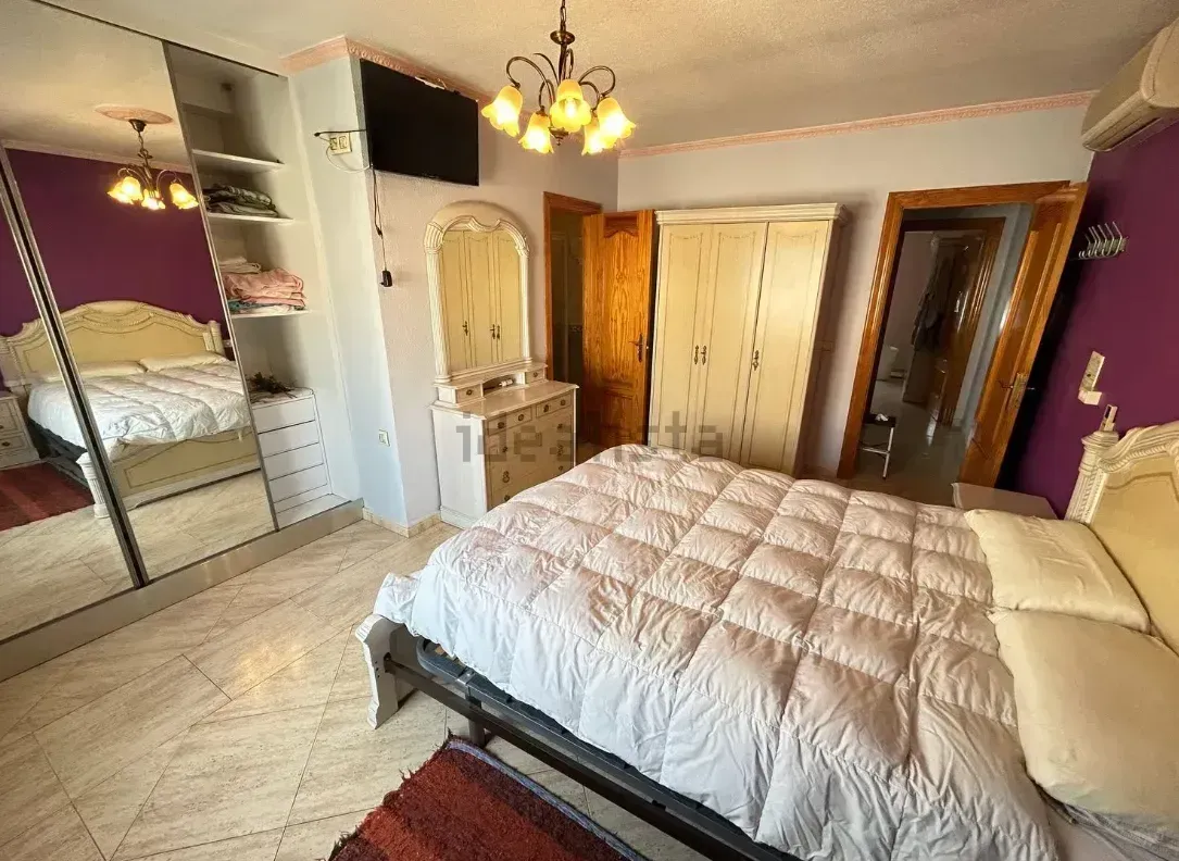 Dormitorio con cama, armario, cómoda, espejo y televisión. Combinación de colores morado y blanco.