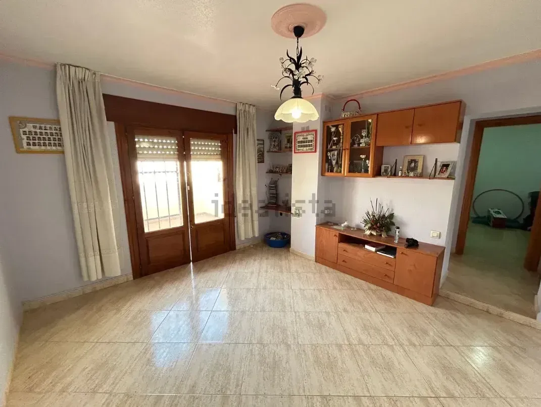 Sala de estar con armarios de madera, ventana/puerta y lámparas. Suelos y paredes de baldosas claras.