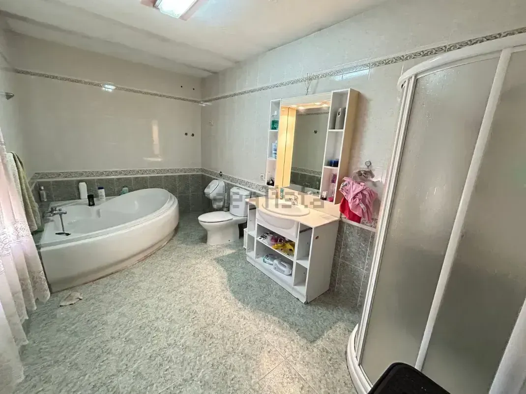 Amplio baño con bañera, ducha, inodoro y tocador con espejo. Tonos azul claro y blanco.