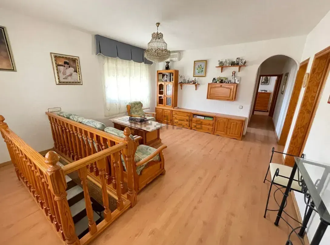 Sala de estar con muebles de madera, escalera y lámpara de araña.