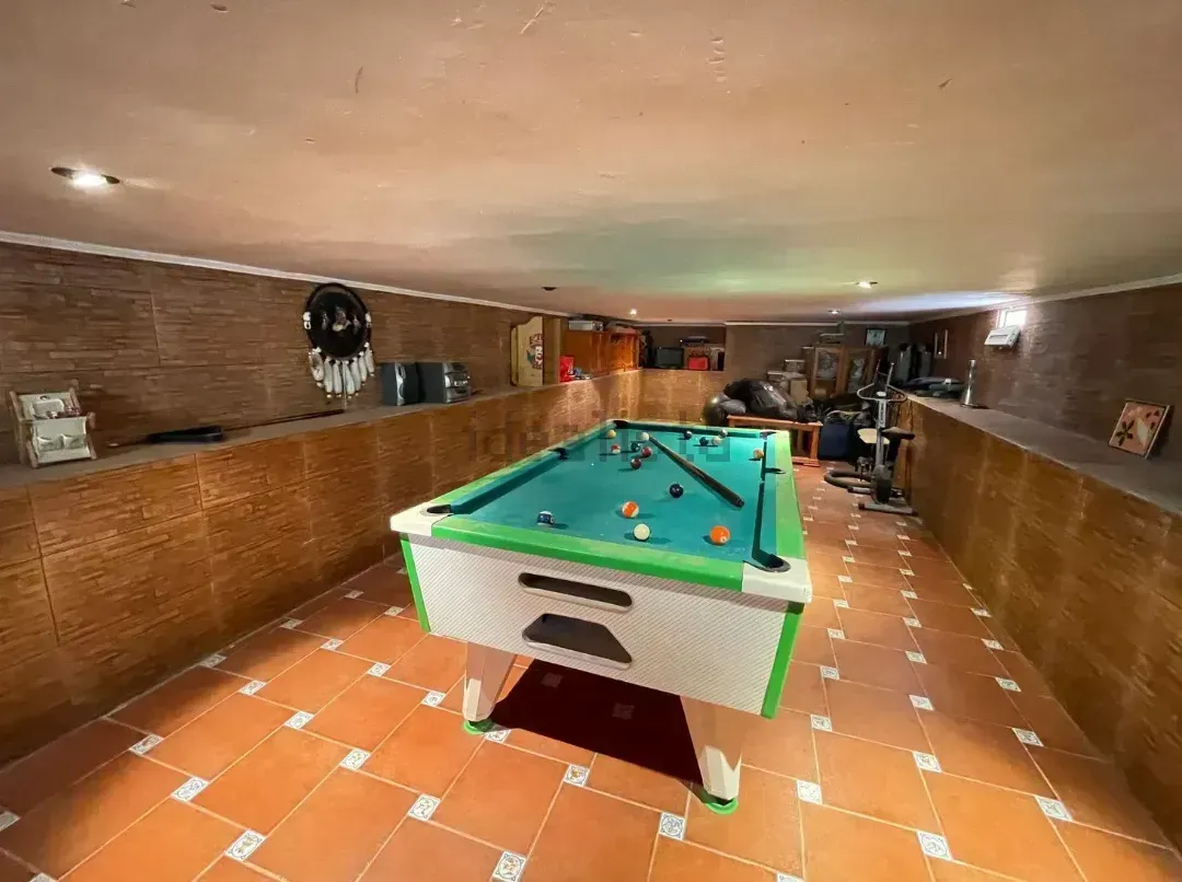 Mesa de billar en una sala de juegos en el sótano con paredes de ladrillo y piso de baldosas.