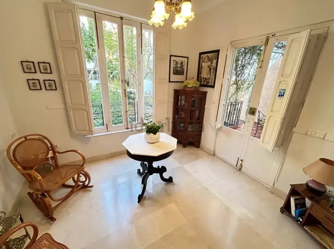 Habitación con paredes blancas, ventanas y muebles antiguos: mesa, silla y mueble.