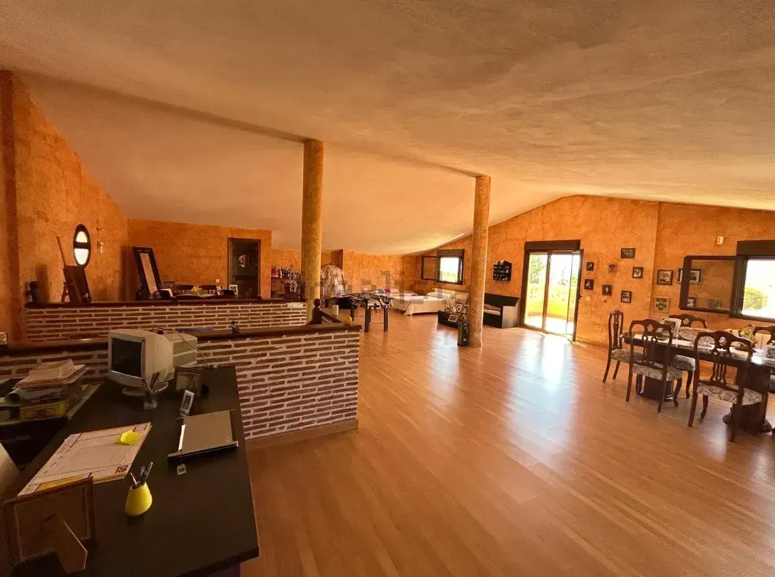 Interior espacioso con paredes naranjas y suelo de madera. Se ven mesas, sillas y una zona de bar.