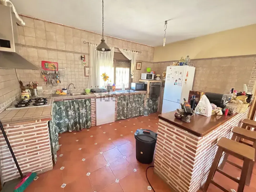 Cocina con detalles de ladrillo, piso de baldosas rojas y barra de desayuno con taburetes.