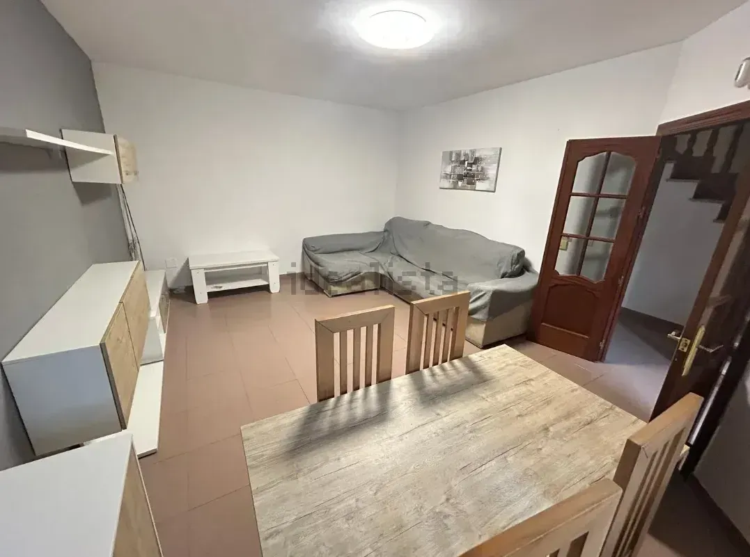 Sala de estar con sofá, mesa de comedor y escaleras. Habitación luminosa en tonos neutros.