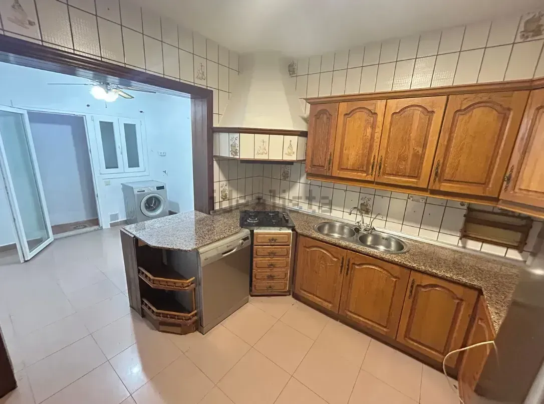 Cocina con gabinetes de madera, encimeras de granito y electrodomésticos de acero inoxidable. Cuarto contiguo con lavandería.