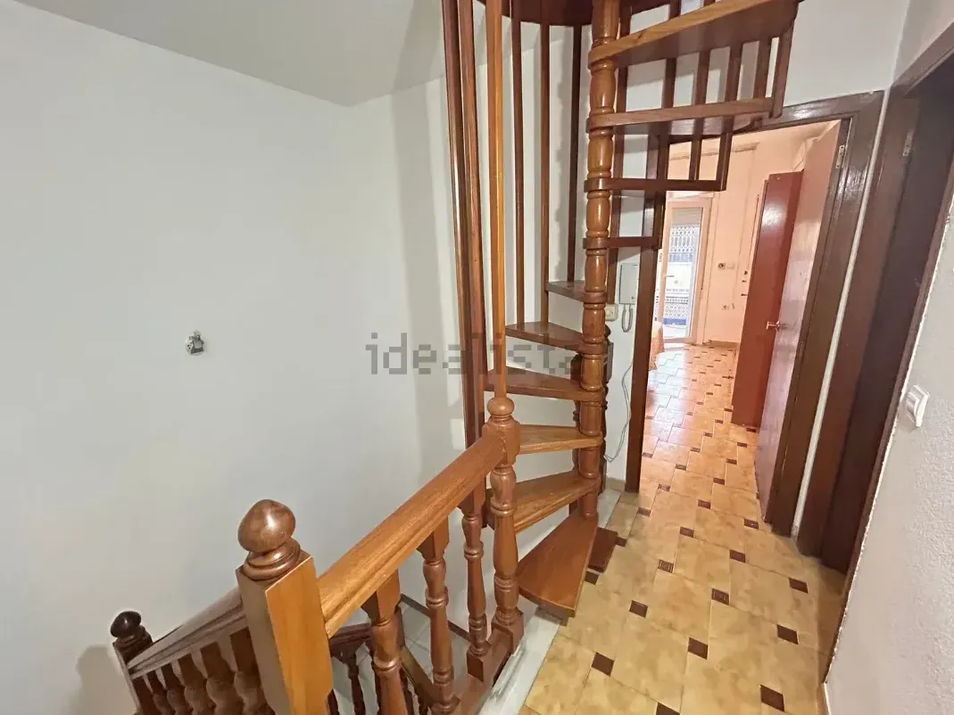 Escalera de caracol de madera en un pasillo con suelo y puertas de baldosas.