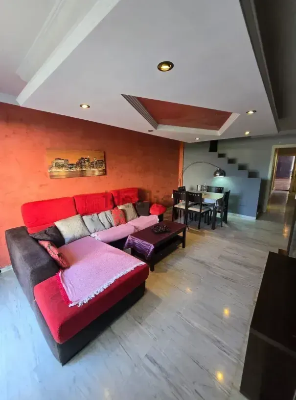 Sala de estar con sofá seccional rojo y marrón, comedor y pisos de mármol.