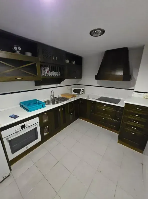 Cocina de madera oscura con encimeras y electrodomésticos blancos; incluye botellero y campana extractora.