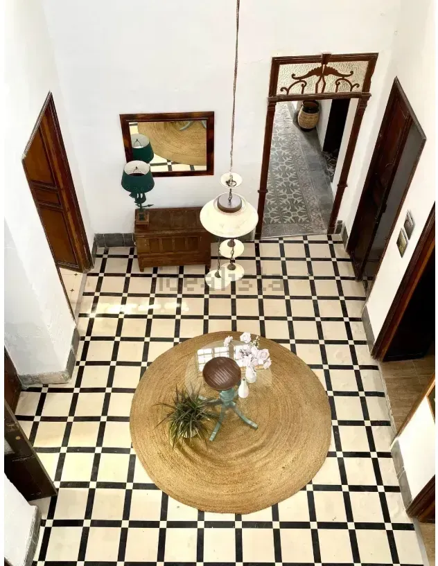 Vista en ángulo alto de una entrada de azulejos con una alfombra redonda, una lámpara colgante y muebles de madera antiguos.