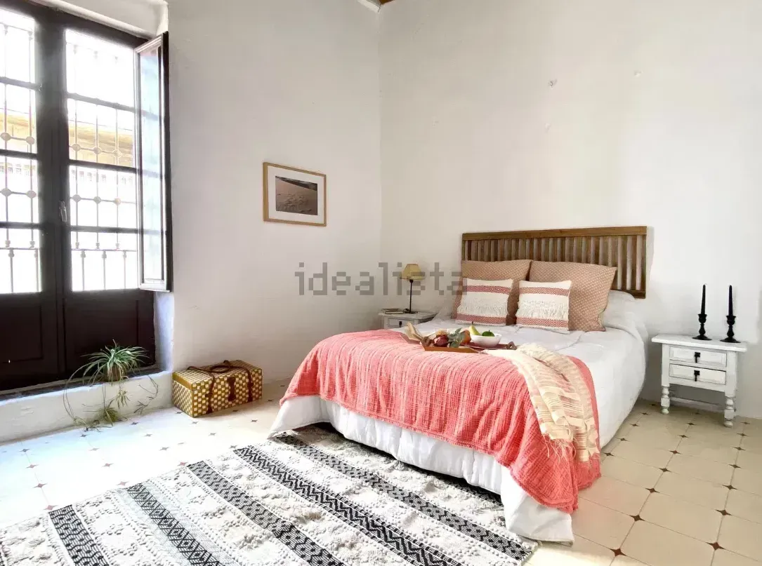 Dormitorio con cama, alfombra y ventana con luz natural. Decoración rosa y blanca.