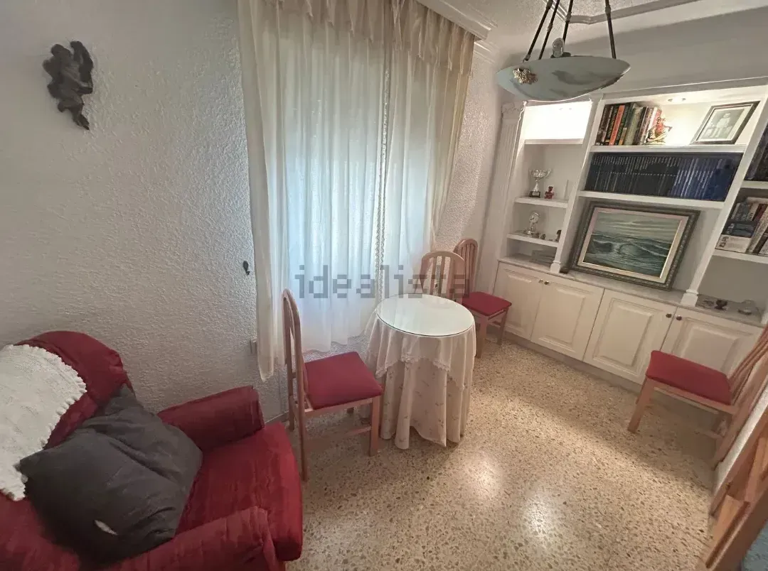 Una acogedora sala de estar con muebles rojos, una mesa pequeña y un armario empotrado; paredes y cortinas blancas.