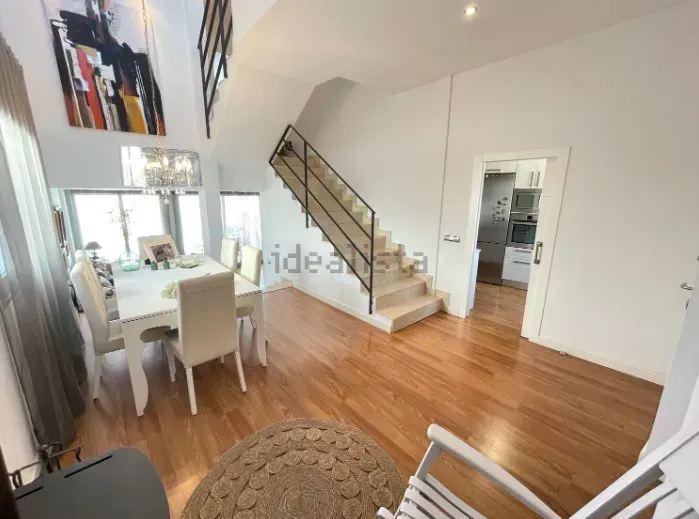 Interior luminoso con zona de comedor, escaleras y puerta de entrada a la cocina.