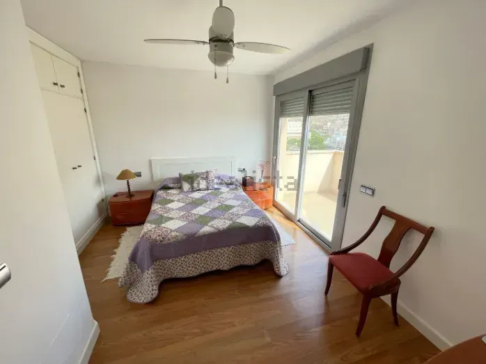 Dormitorio con piso de madera, cama con edredón, armario blanco y acceso al balcón.