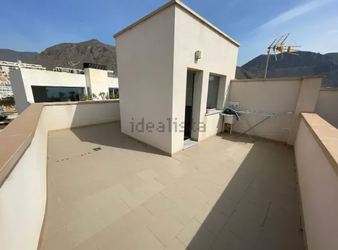 Terraza en la azotea con un pequeño edificio, paredes beige y fondo de montaña.