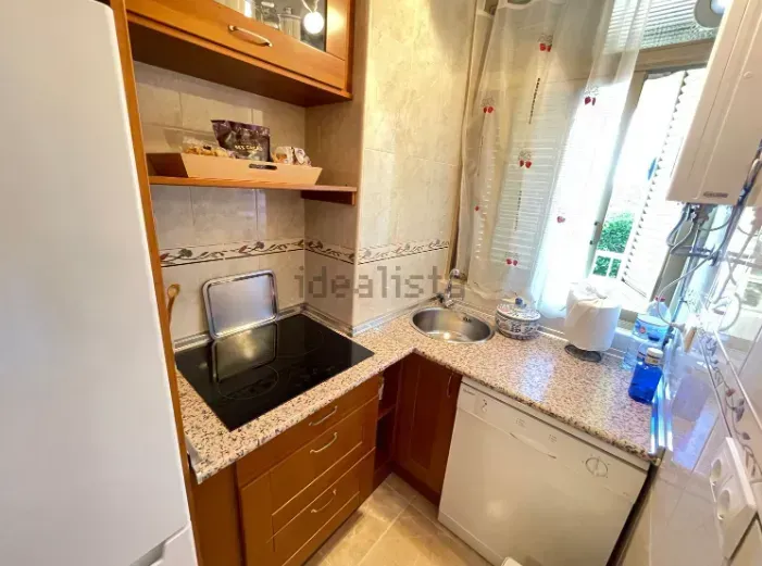 Pequeña cocina con gabinetes de madera, encimeras de granito y un fregadero junto a una ventana.