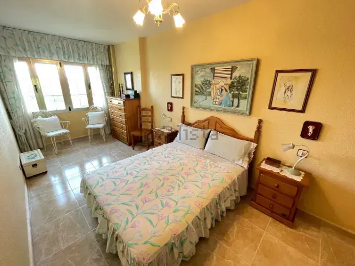 Dormitorio con cama, mesita de noche, cómoda, obras de arte y una ventana con luz natural.