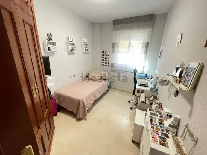 Dormitorio con cama, escritorio y armario contra paredes de color gris claro.