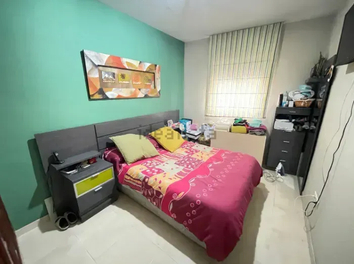 Dormitorio con pared verde, cama con ropa de cama rosa, cabecero gris, mesita de noche y ventana.