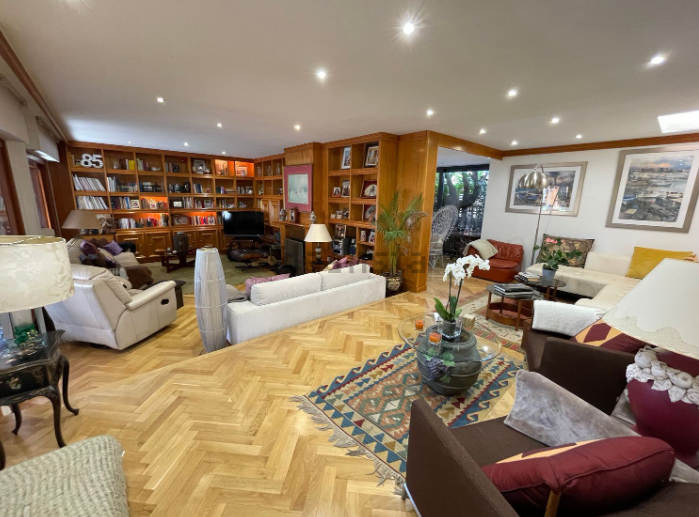 Amplia sala de estar con estantes de madera llenos de libros, varias disposiciones de asientos y pisos de parquet.