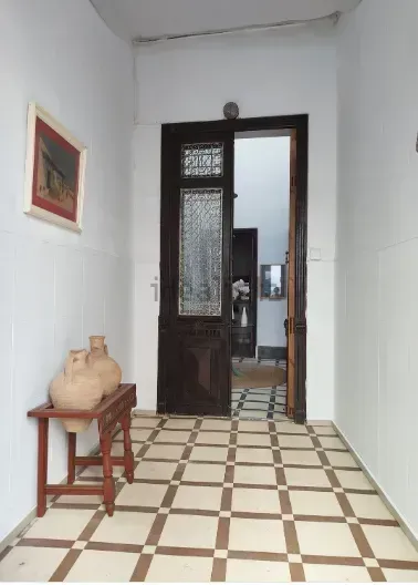 Pasillo con suelo ajedrezado, puerta de madera marrón y mesa pequeña con jarrones.