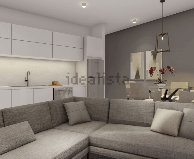 Espacio habitable moderno con cocina blanca, sofá seccional gris y comedor.