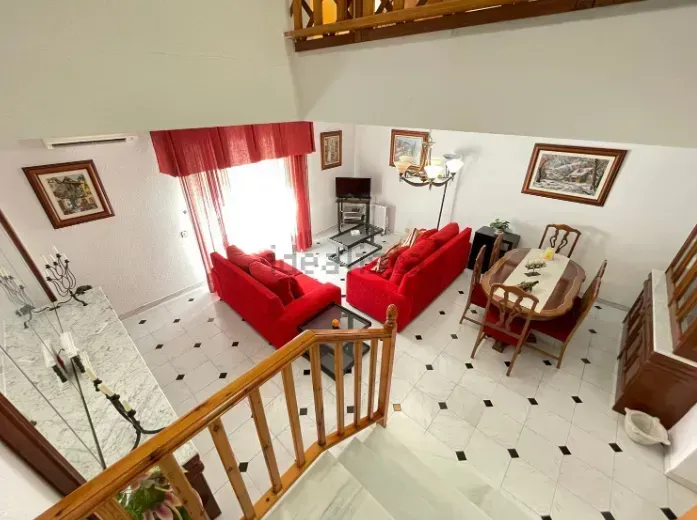 Sala de estar con sofás rojos, mesa de comedor redonda y escalera, tomada desde arriba.