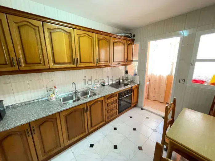 Cocina con gabinetes de madera, fregadero de acero inoxidable, encimera y mesa de comedor.