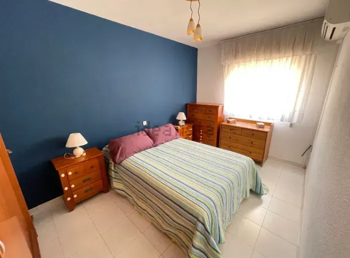 Dormitorio con pared de acento azul, muebles de madera y ropa de cama a rayas.