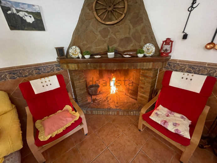 Dos sillones rojos se sitúan frente a una chimenea encendida en un hogar de piedra.