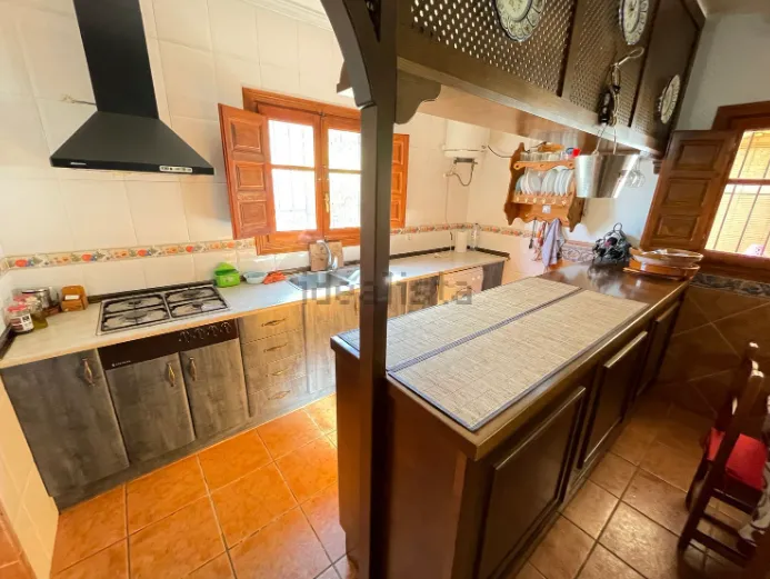 Cocina con muebles de madera, estufa a gas, piso de terracota y ventana abierta con contraventanas.