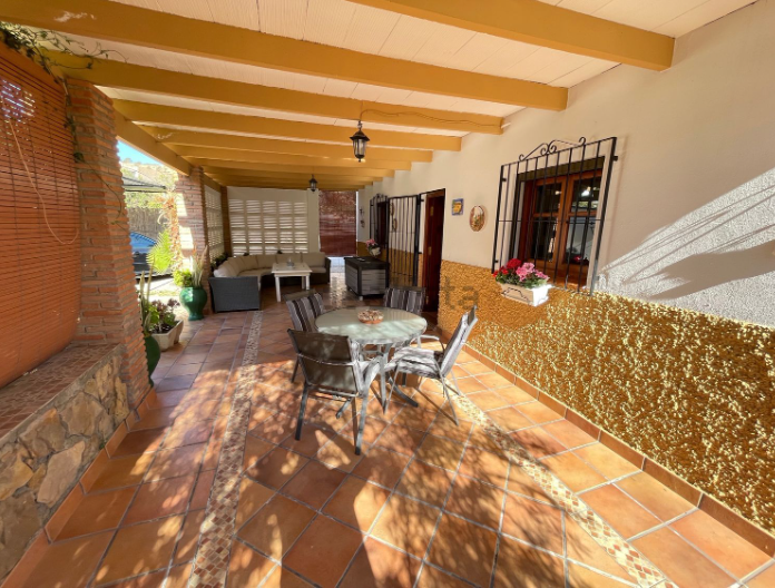 Patio cubierto con asientos: mesa redonda y sillas, piso de ladrillo color canela, paredes texturizadas amarillas.