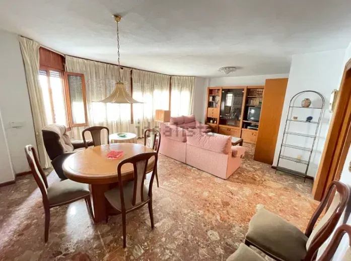Sala de estar con mesa de comedor, sofá rosa y armario empotrado de madera. Suelo de mármol.