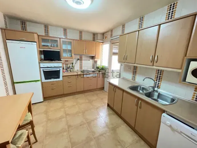 Cocina con gabinetes de color marrón claro, electrodomésticos y salpicadura de azulejos.