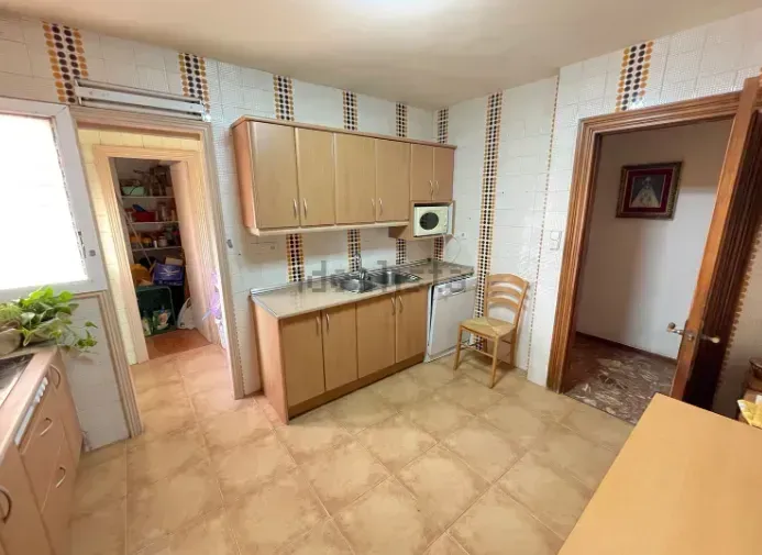 Cocina con gabinetes de madera clara, paredes revestidas de azulejos y una puerta que conduce a otra habitación.