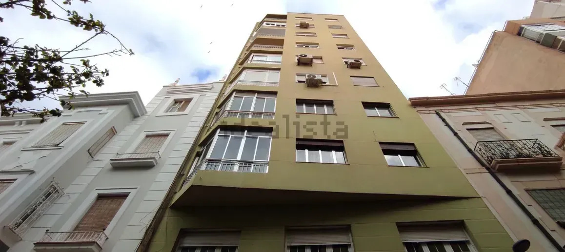 Edificio alto de apartamentos de color verde claro con aire acondicionado y ventanas. Otros edificios a ambos lados.