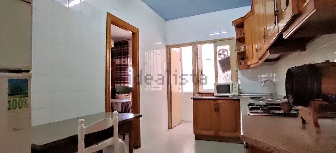 Interior de cocina con techo azul claro, gabinetes de madera y puerta a un comedor con mesa y silla.
