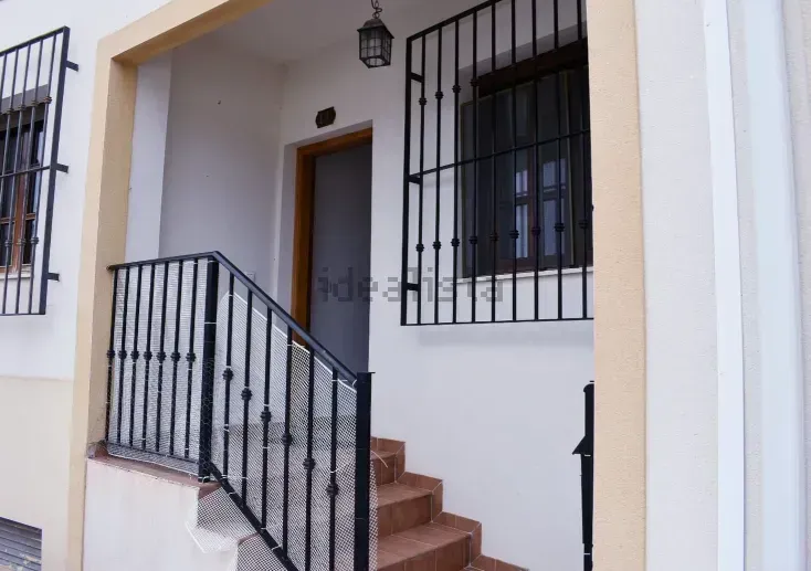 Exterior de un edificio con escalones, rejas de hierro forjado negro en ventanas y barandilla y exterior de color claro.