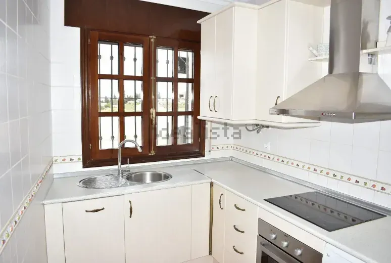 Cocina con gabinetes blancos, electrodomésticos de acero inoxidable y una ventana con marco marrón.