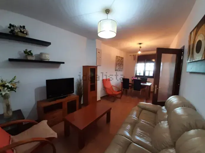 Sala de estar con sofá, TV y comedor. Muebles de madera, paredes neutras y silla naranja.