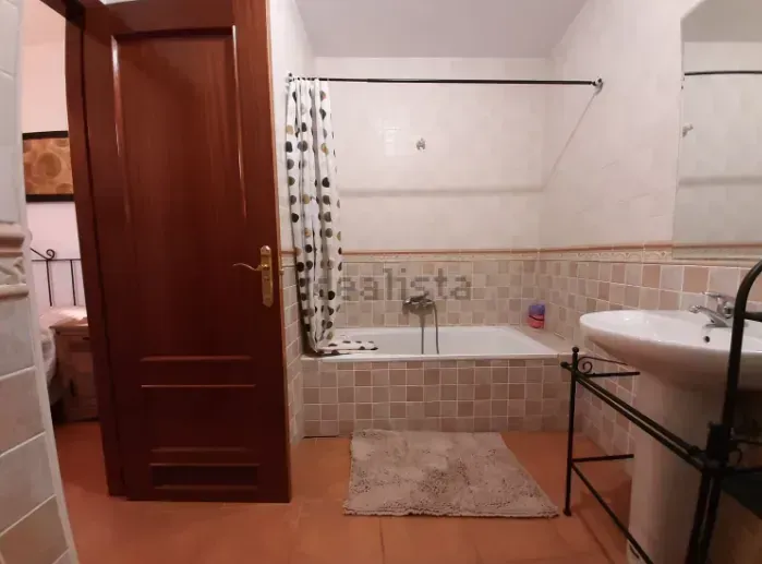 Baño con bañera, lavabo y puerta marrón. Paredes y suelo de azulejos beige.