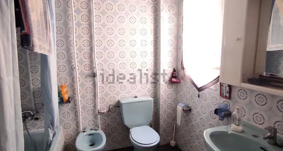 Baño con azulejos estampados, inodoro, bidé, lavabo y cortina de ducha. La luz natural entra a raudales por la ventana.