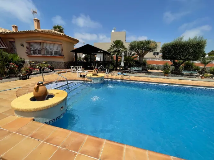 Un patio trasero con piscina, cenador y casa bajo un cielo azul.