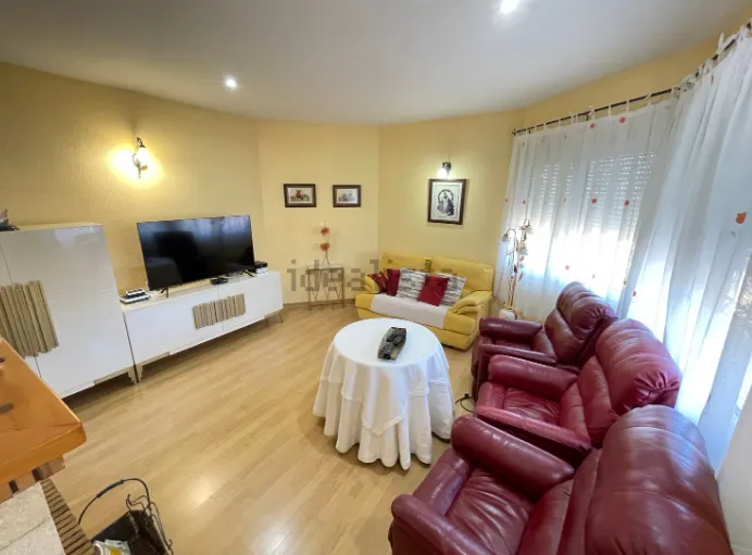 Sala de estar con sofás rojos y amarillos, TV, mesa redonda y suelo de madera en color claro.