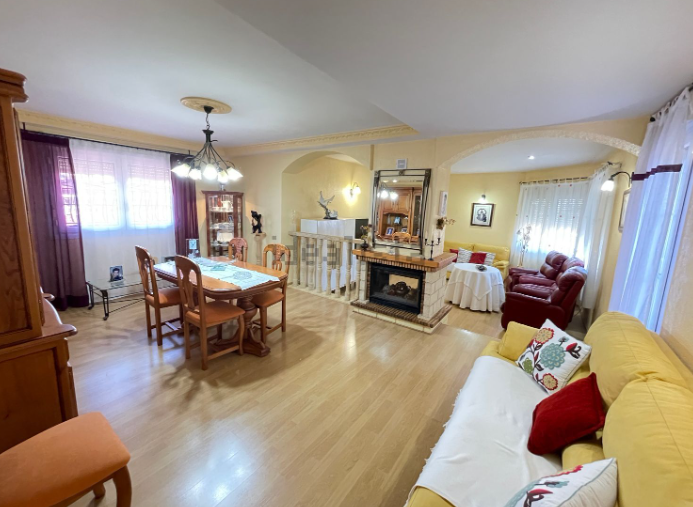 Sala de estar con comedor, chimenea y muebles; pisos de madera clara, paredes amarillas y grandes ventanales.