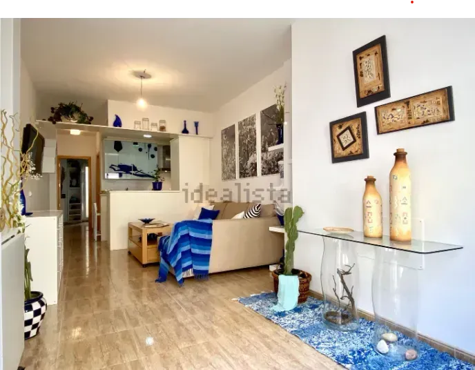 Sala de estar con sofá beige, detalles azules, mesa de vidrio y arte decorativo de pared.